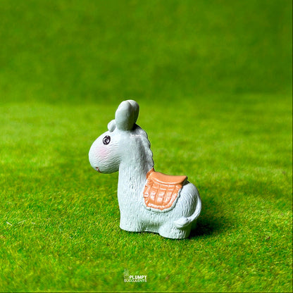 Small white donkey figurine with a pink saddle on a green grass-like background